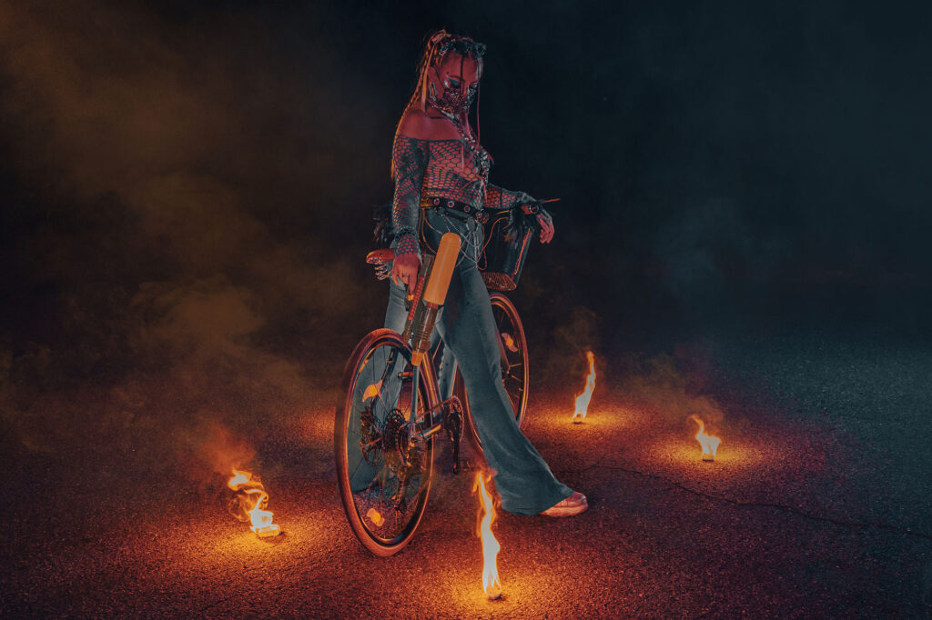 Model with a bicycle among fires at night — Burning Man series