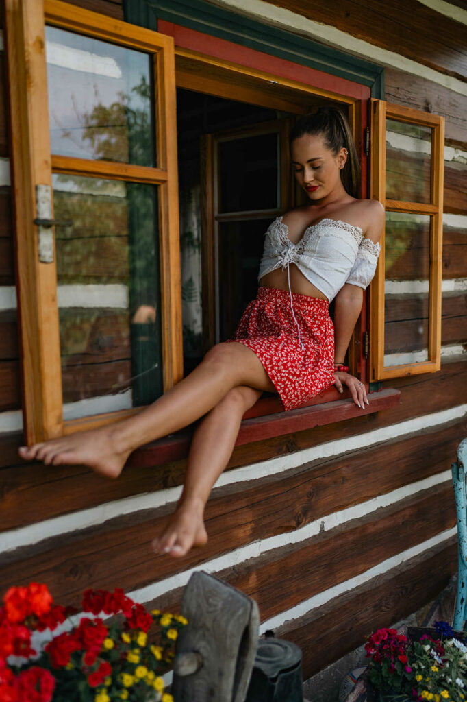 Young woman in a folk costume sitting in the window of an old cottage, welcoming the morning, HotFolk calendar