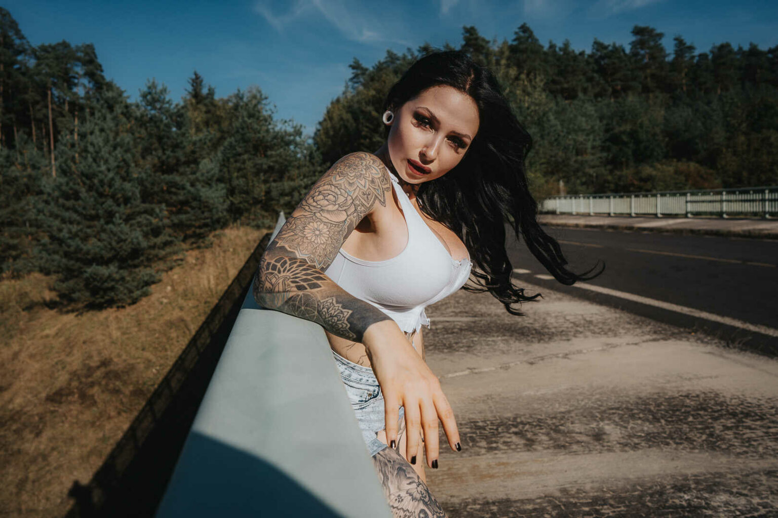 Tereza in a white top on a road barrier with pine hills behind