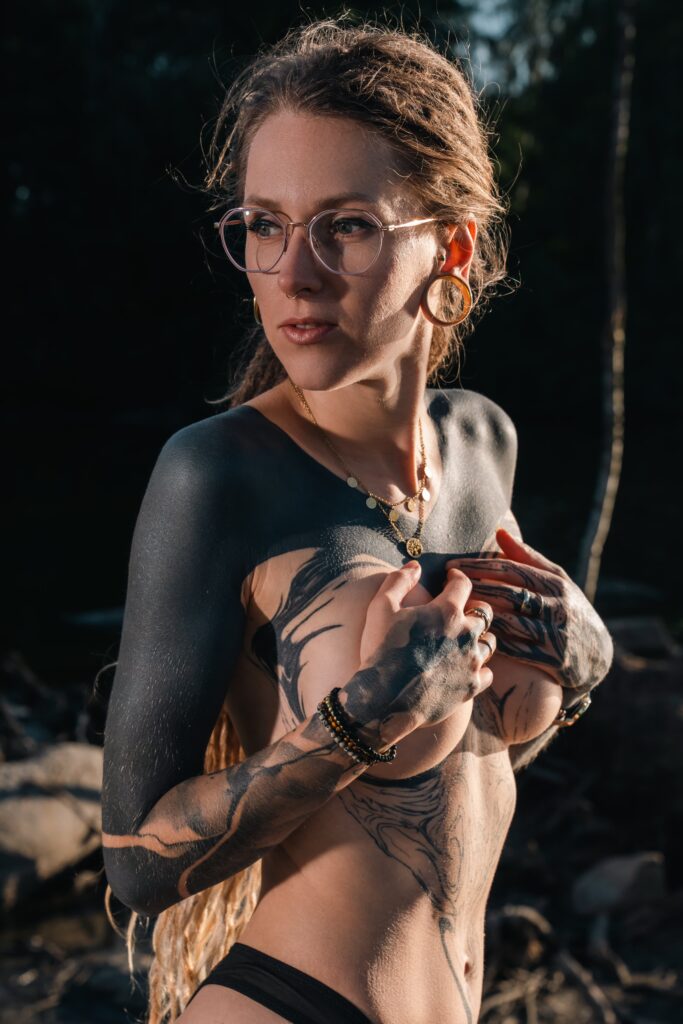 Naira.Sax, tattooed model with dreadlocks, photographed by a pond during golden hour.
