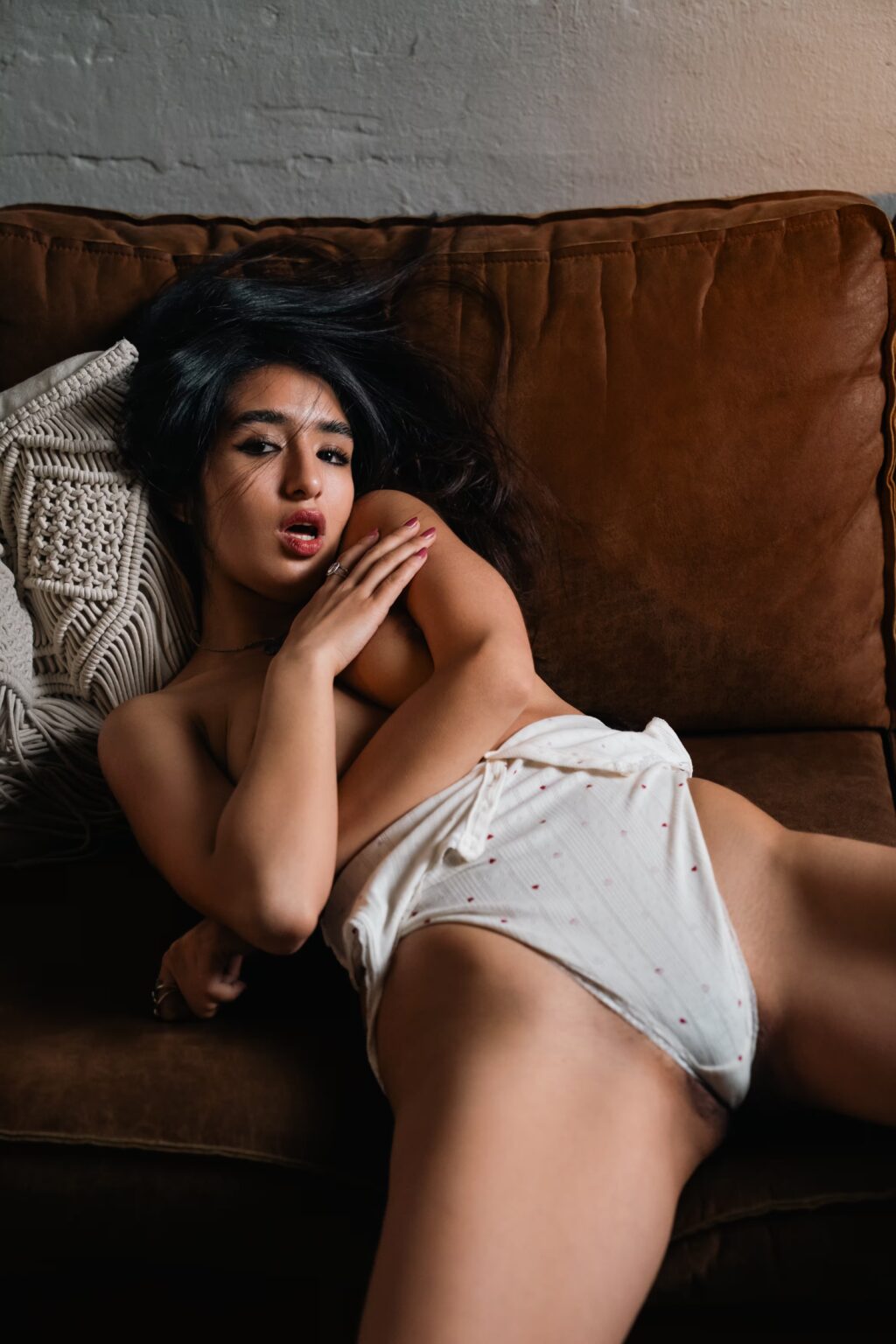 Sofia lying topless on a brown sofa in white lace