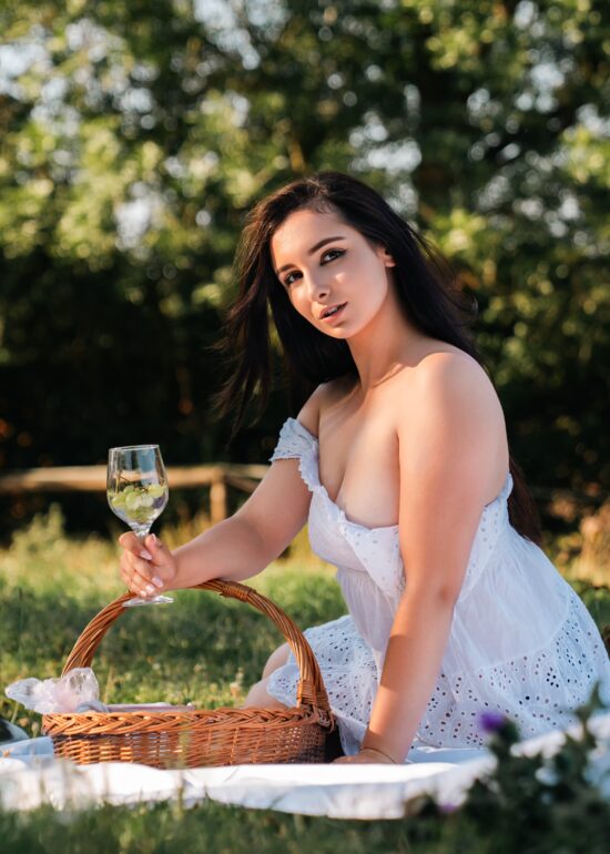 Nikol relaxing on a picnic blanket in a green garden with a white horse in the background.