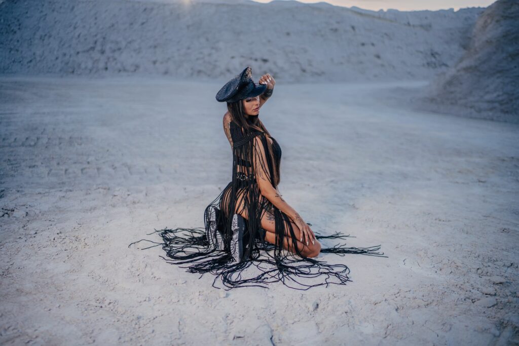 Jana kneeling in desert sand, Gurning Man-inspired costume, sunlight casting long shadows