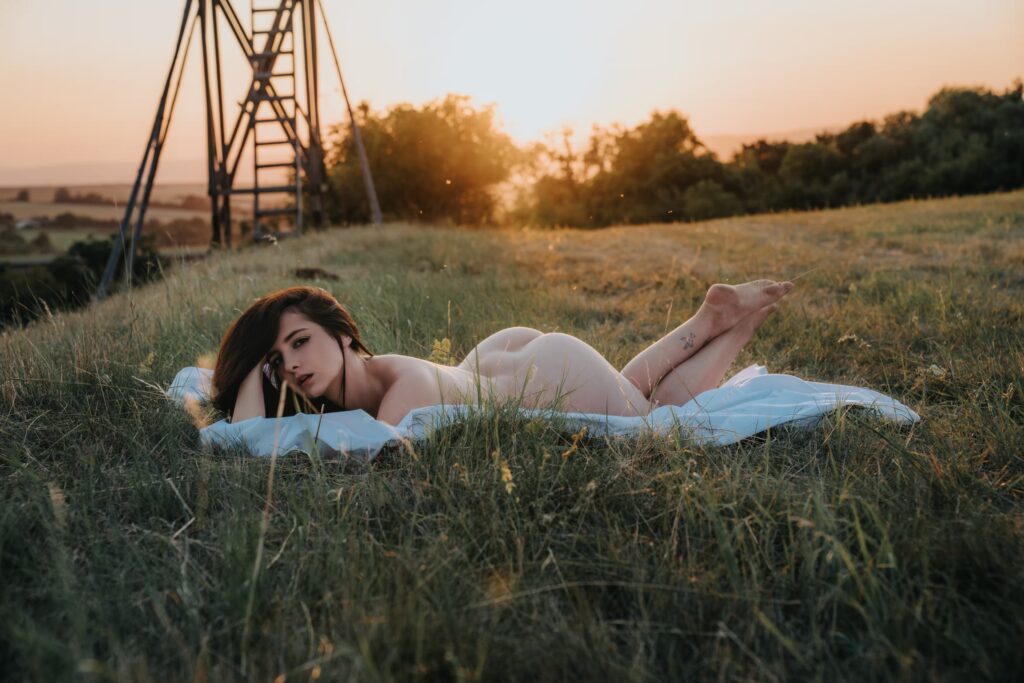 Nikol lying nude on a blanket in a meadow at golden hour