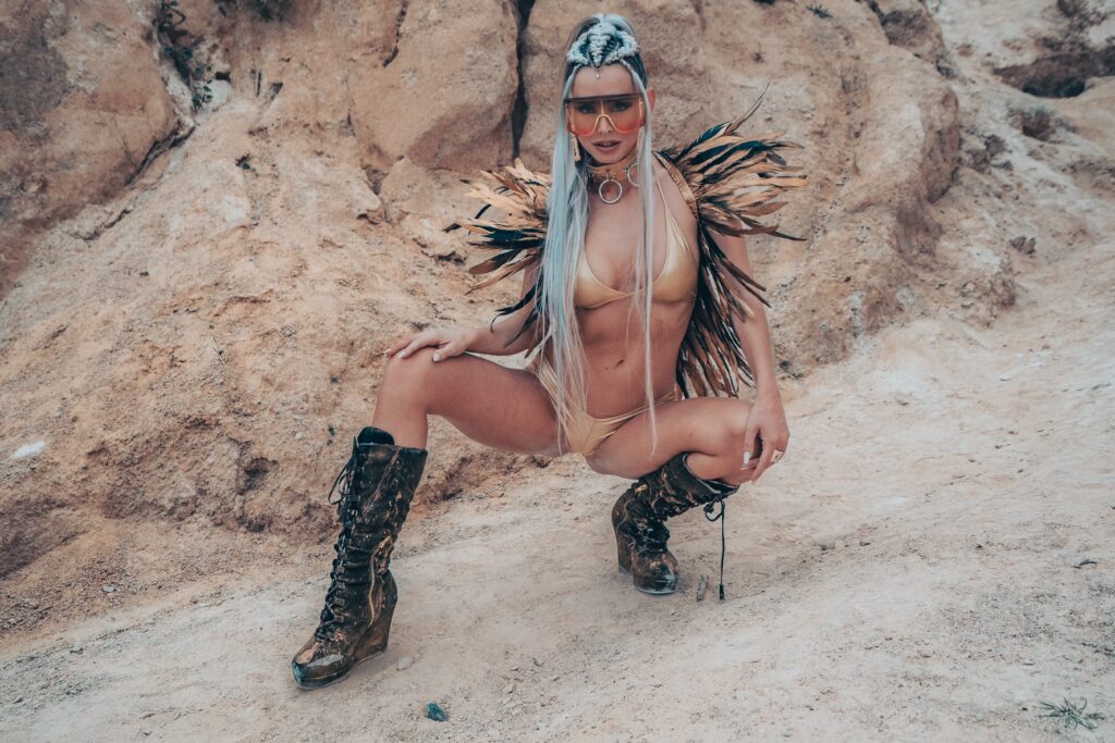 Model in feathers and boots crouching in a desert-like quarry – Burning Man series