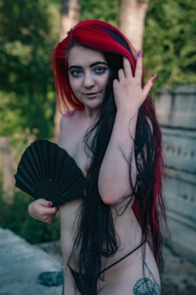 Natali with red hair covering her body with a black fan