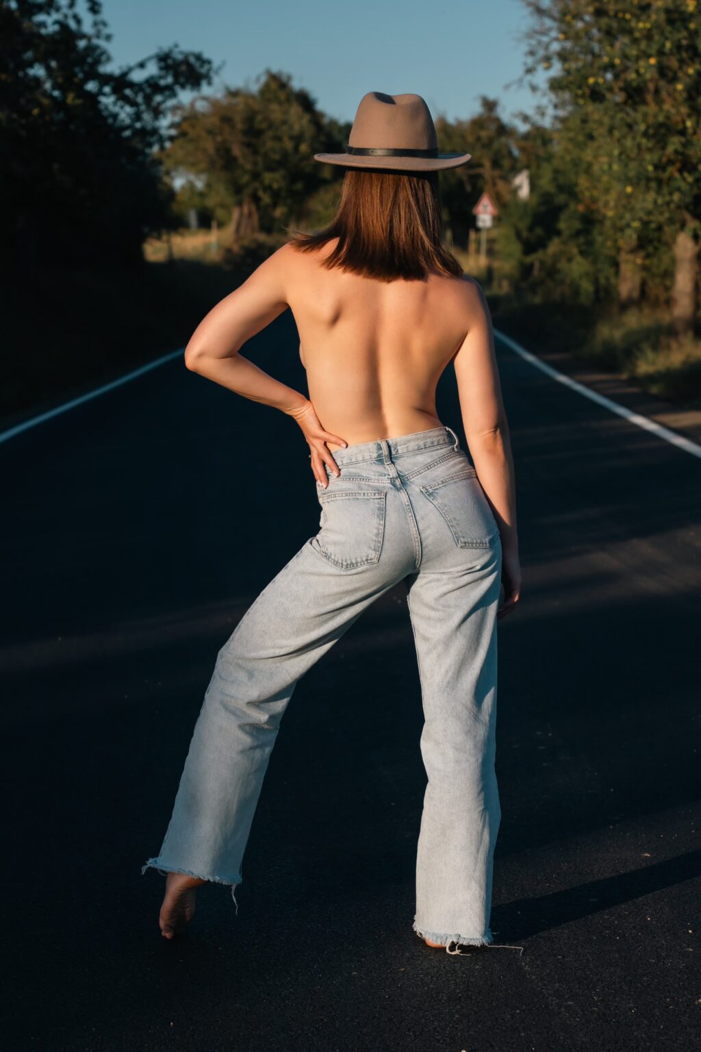 Won't Tell You in jeans and a hat seen from behind on an empty road