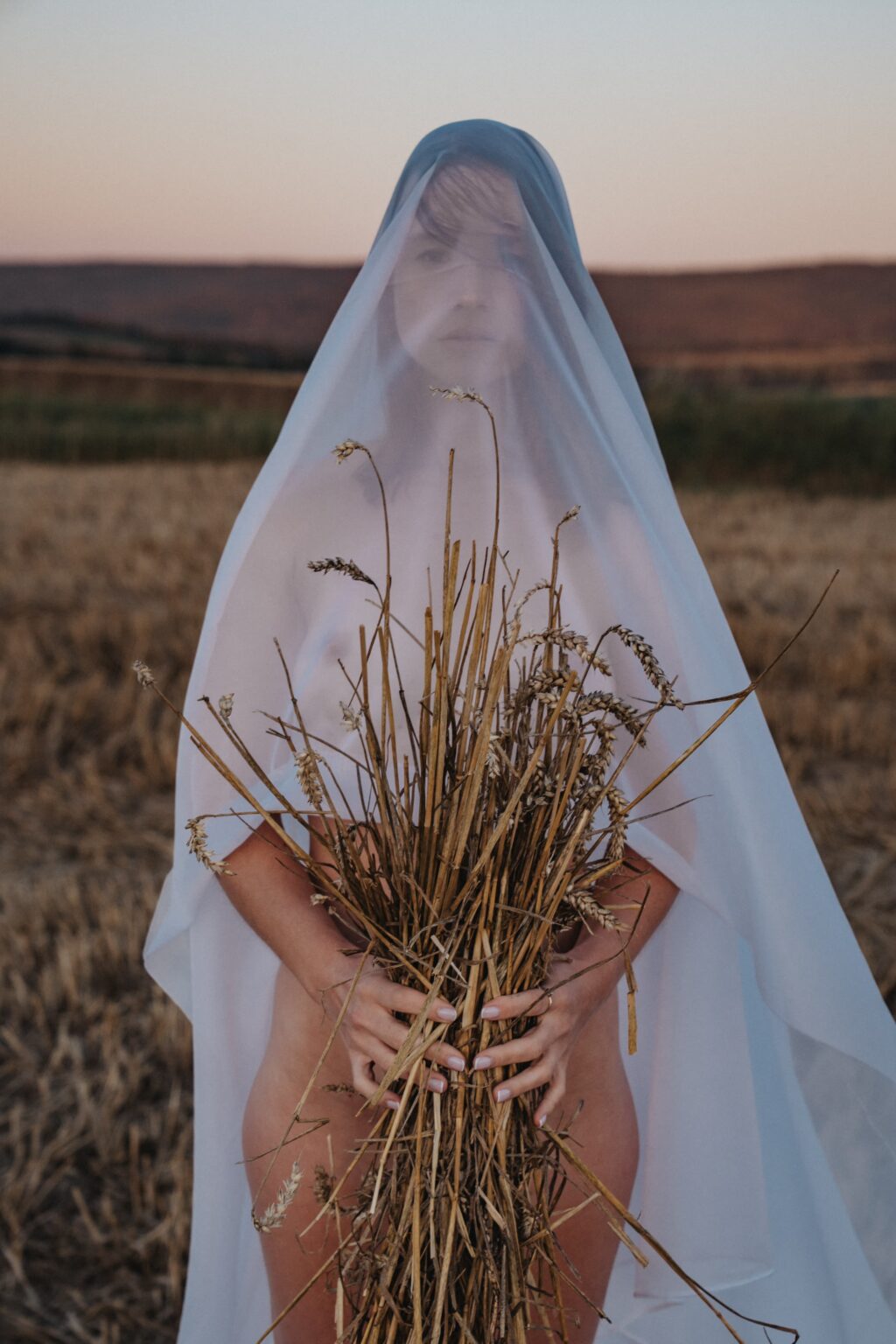 Won't Tell You under a white veil holding straw in a field