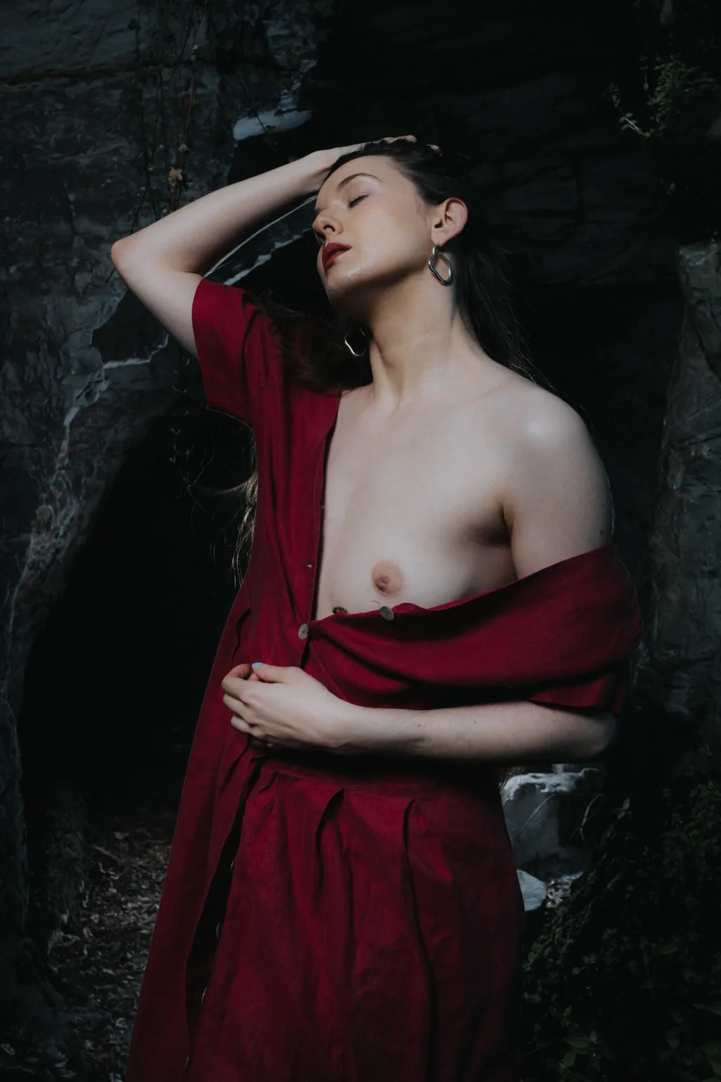 Anna with a red dress slipping off her shoulders against a dark tree