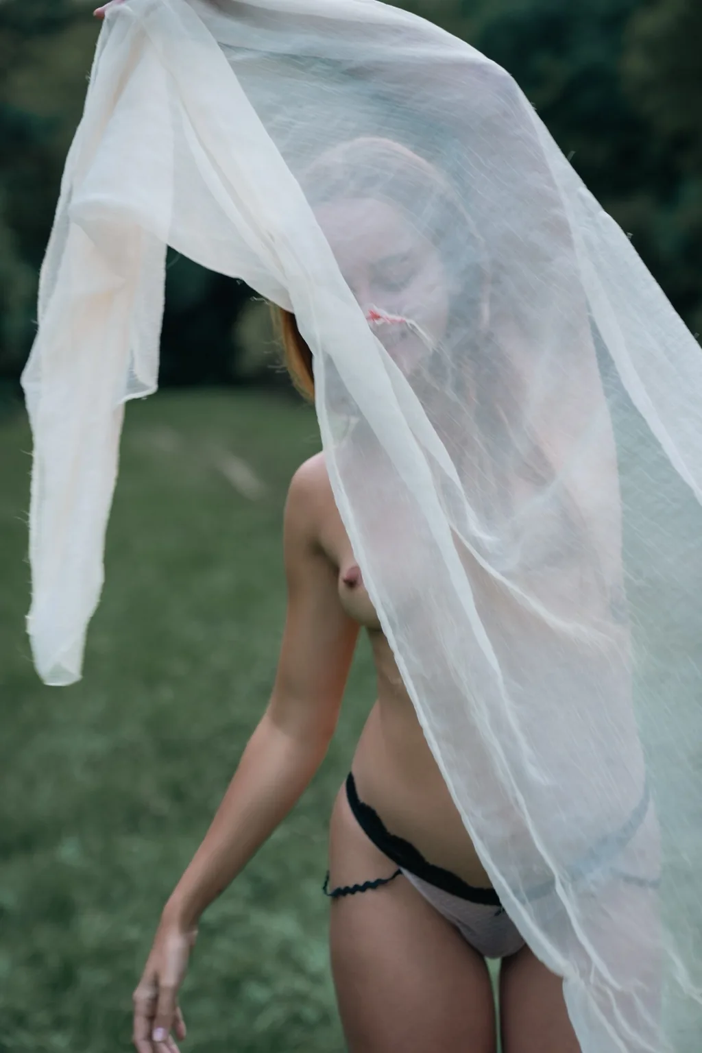 Mellisa from behind lifting a sheer white veil in a park