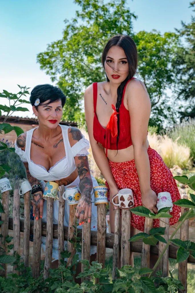 Two models in folk outfits leaning on a wooden fence with mugs, HotFolk 2027 calendar