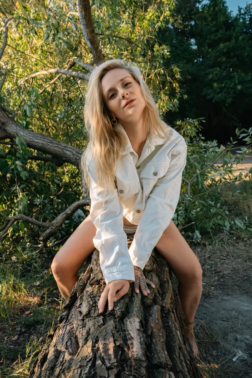 Cami Fox, blonde model in a white shirt sitting on a tree stump in the forest, golden hour