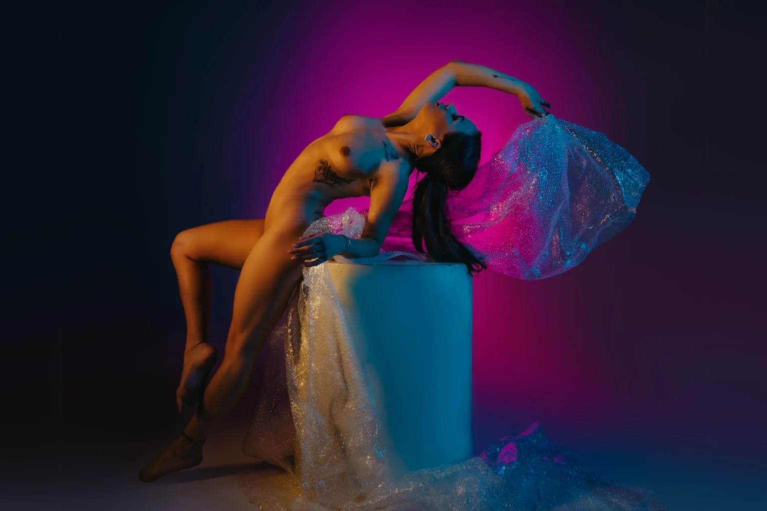 Martina arching back on a white plinth in purple and red light