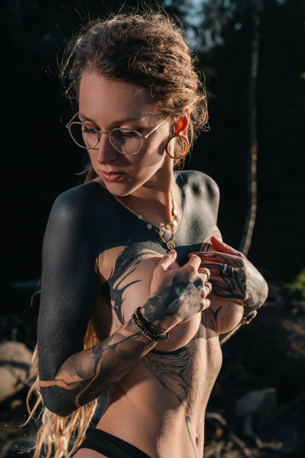 Naira Sax in glasses covering her chest, tattooed arms